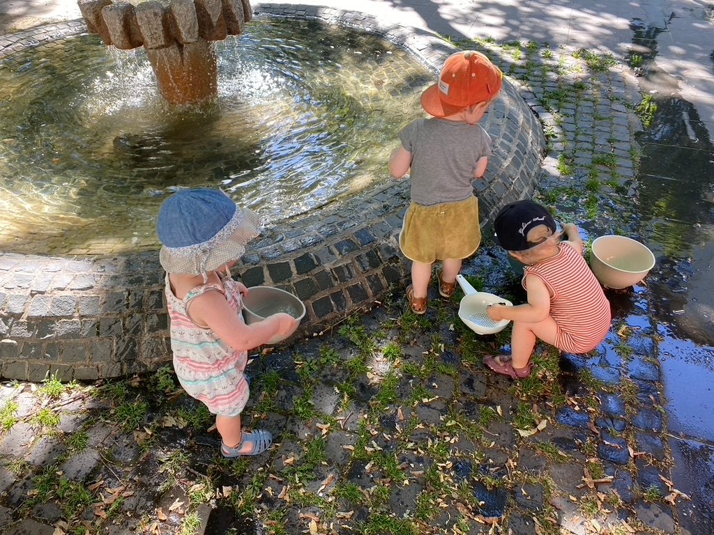 Drei Kinder spielen mit Wasser am Brunnen