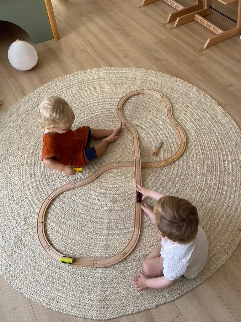 Zwei Kinder spielen mit der Holzeisenbahn auf dem Teppich