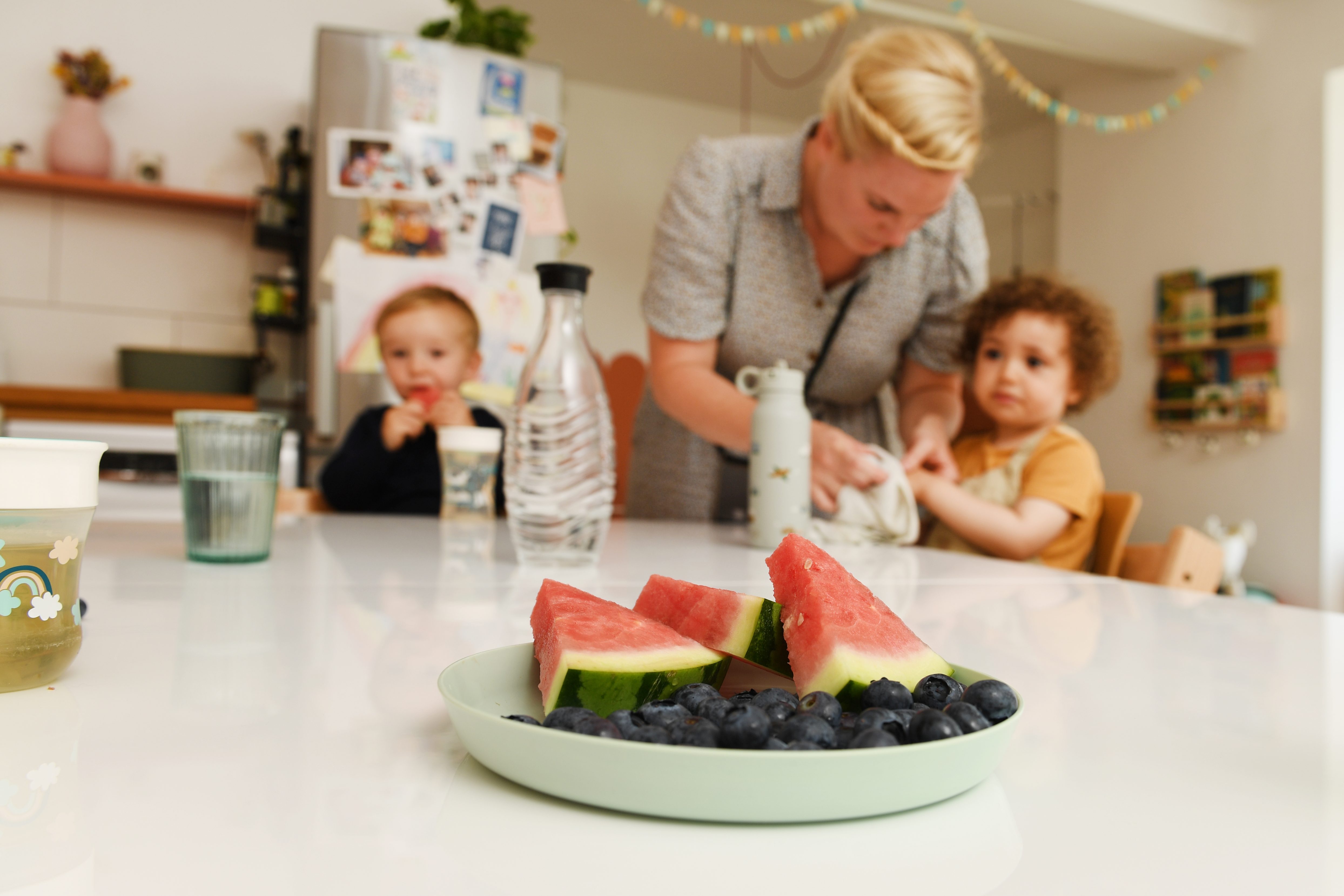 Tita bereitet Obst zu, zwei Kinder warten am Tisch
