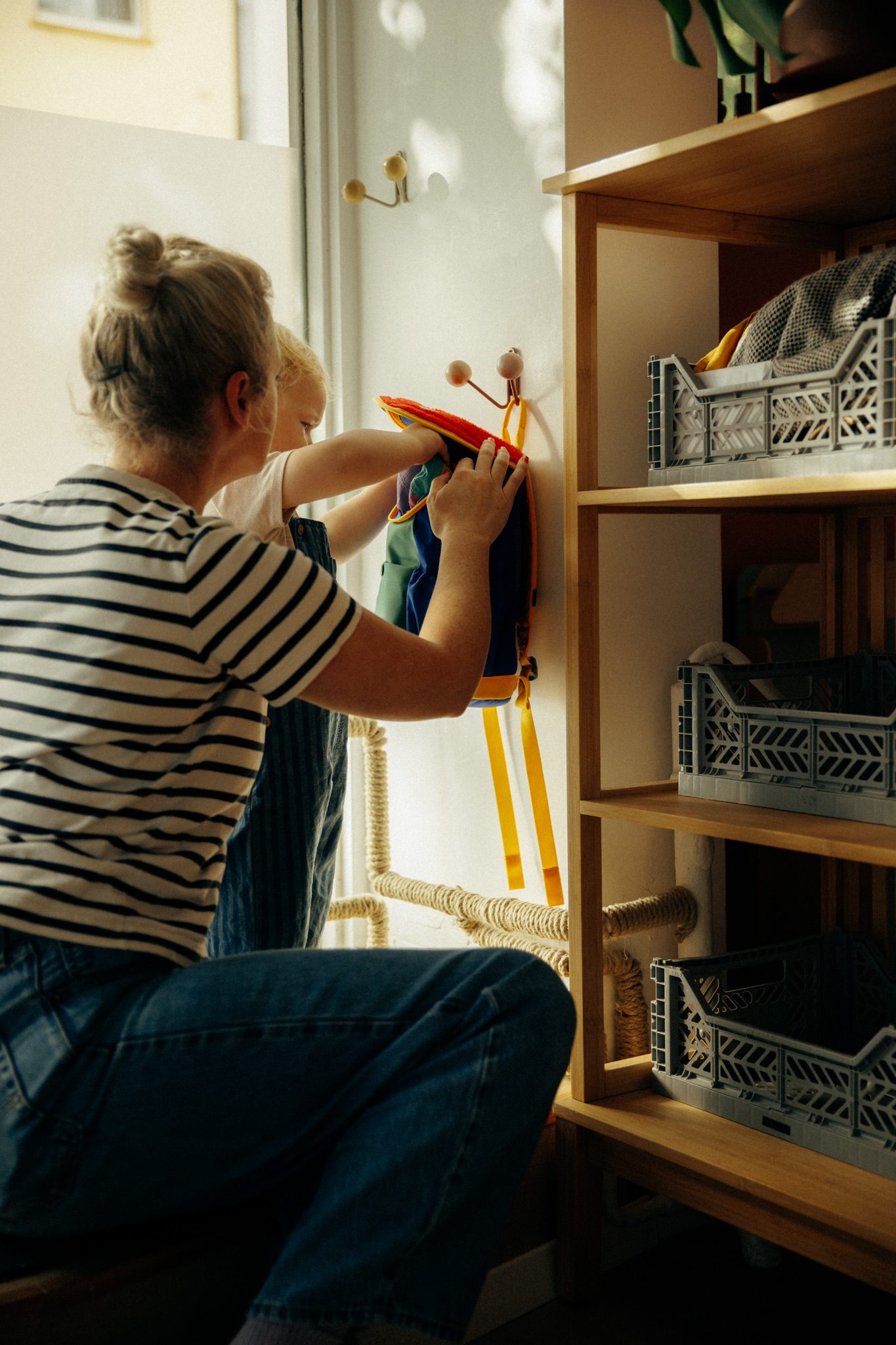 Tita hilft einem Kind, den Rucksack an die Garderobe zu hängen