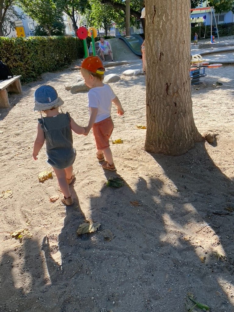 Zwei Kinder spazieren Hand in Hand auf dem Spielplatz