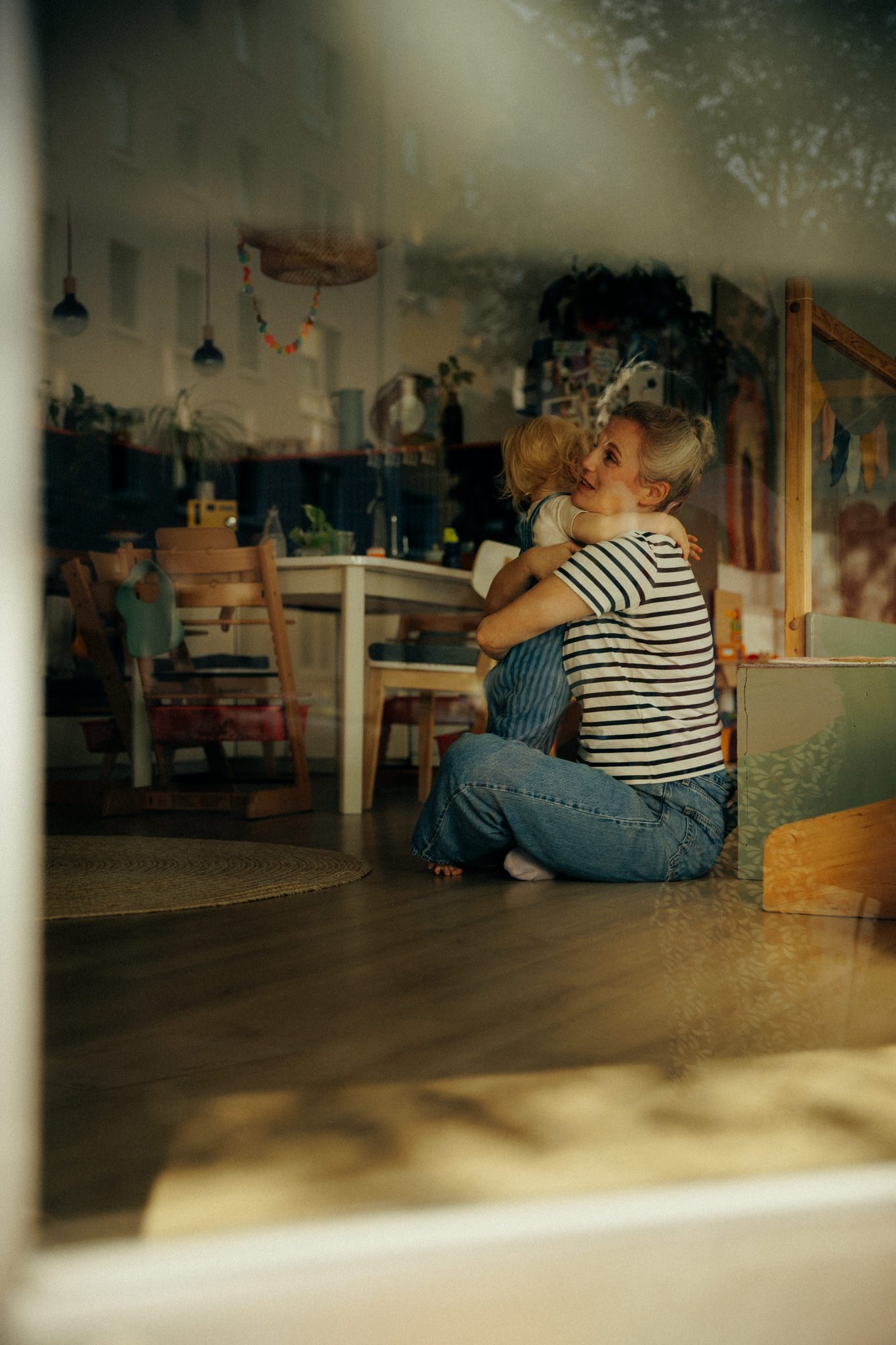 Tita umarmt ein Kind, Spiegelung im Fenster